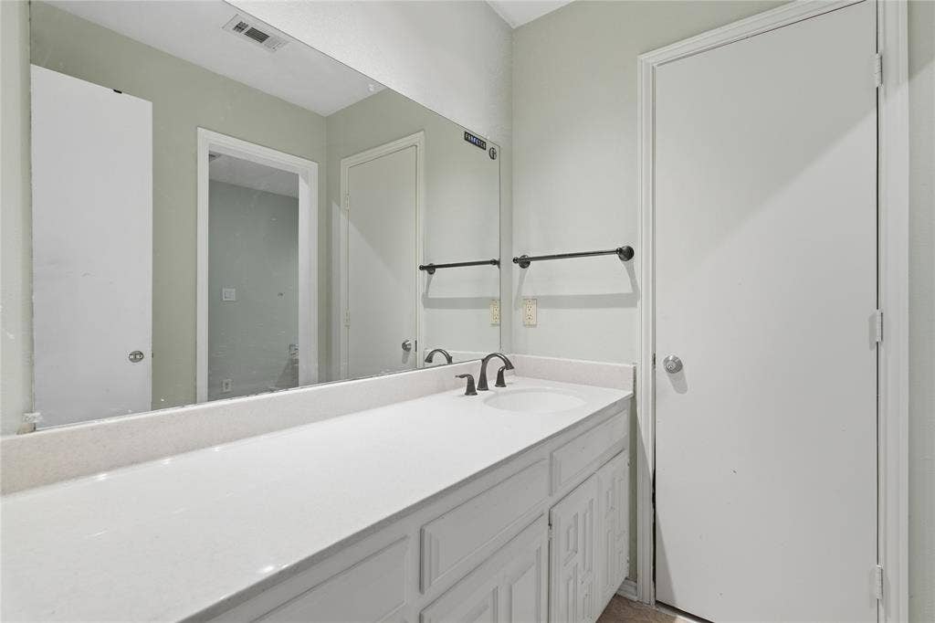 1010 Florence Drive, Duncanville, TX 75116 White vanity with integrated sink, dark bronze faucet, and expansive wall-mounted mirror