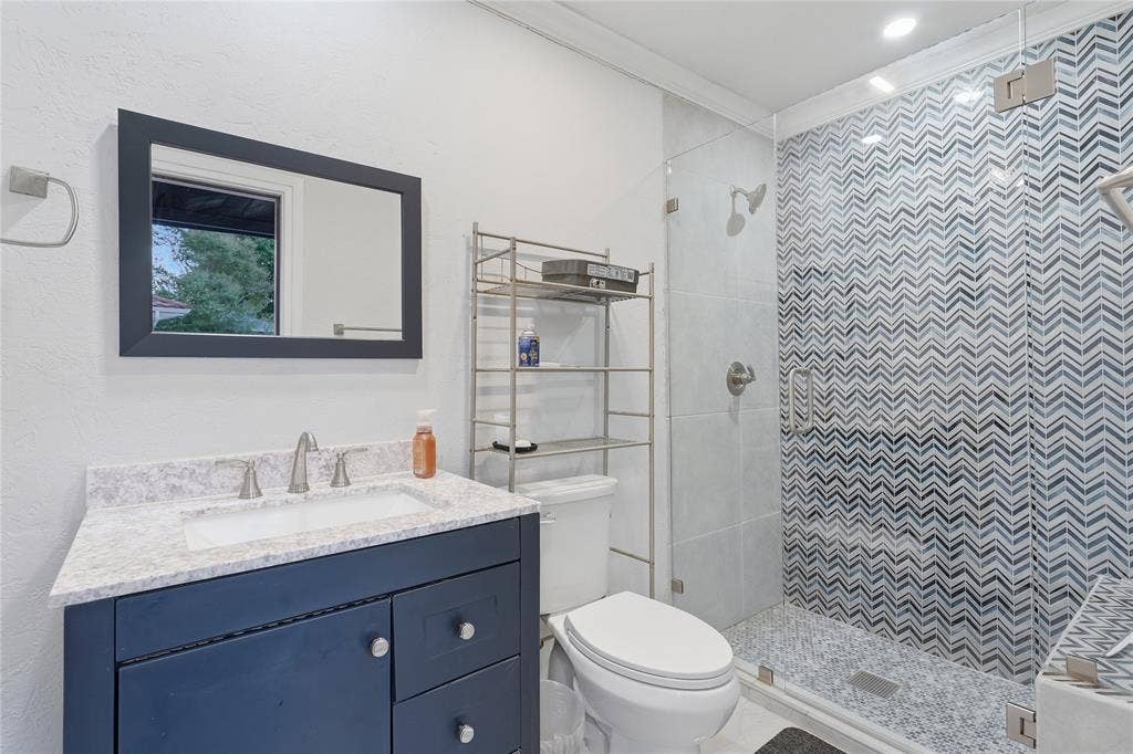 1010 Florence Drive, Duncanville, TX 75116 Bathroom featuring a glass-enclosed shower with chevron-patterned tile, a dark-toned vanity with a light-toned countertop, and recessed lighting