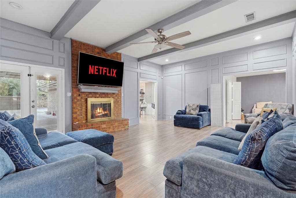 1010 Florence Drive, Duncanville, TX 75116 Brick fireplace with a brass firebox, ceiling fan, wood-finish flooring, and decorative wall paneling