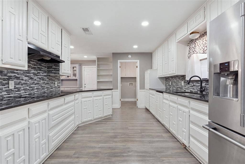 1010 Florence Drive, Duncanville, TX 75116 Well-appointed kitchen featuring extensive white cabinetry, dark countertops, a tiled backsplash, wood-finish flooring, and recessed lighting