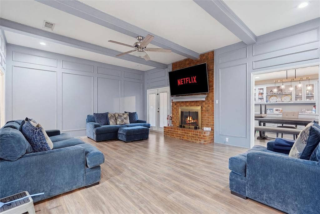 1010 Florence Drive, Duncanville, TX 75116 Spacious living area featuring wood-finish flooring, a brick fireplace with a mantel, and decorative paneling