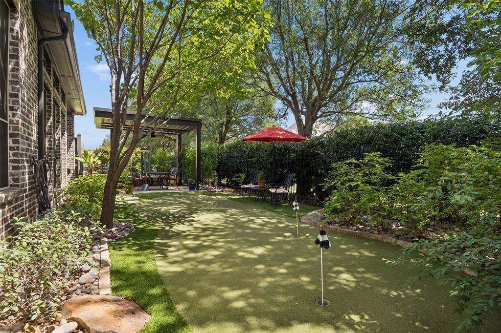 6009 Heron Bay Lane, McKinney, TX 75070 Backyard retreat with a putting green and treed privacy fence line.
