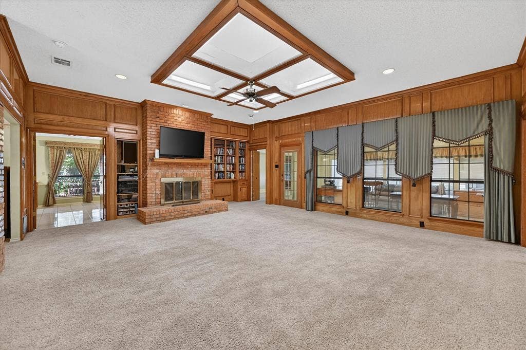 206 Harris Drive, Sunnyvale, TX 75182 Carpeted living area featuring a brick fireplace, built-in shelving, wood wall paneling, and a coffered ceiling with skylights