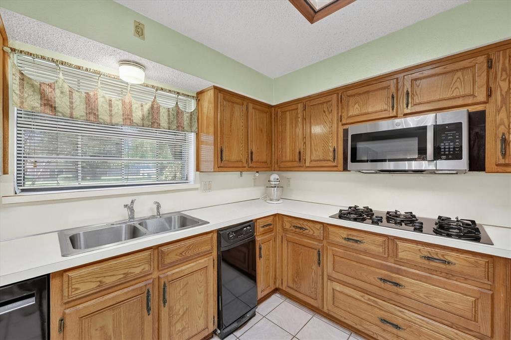206 Harris Drive, Sunnyvale, TX 75182 Kitchen featuring wood cabinetry, white countertops, a double basin stainless steel sink, a stainless steel microwave, and a four-burner cooktop
