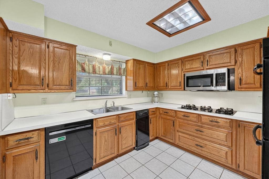 206 Harris Drive, Sunnyvale, TX 75182 Kitchen featuring wood cabinetry, white countertops, a stainless steel microwave, black dishwasher, and white tile flooring