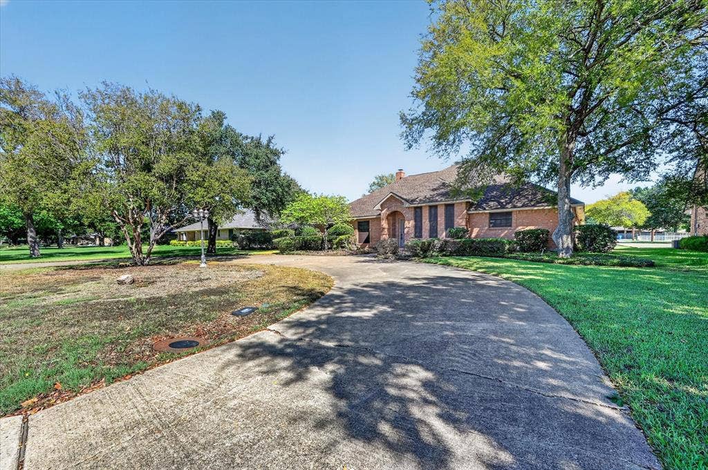 206 Harris Drive, Sunnyvale, TX 75182 Curved concrete driveway with mature trees, brick exterior, and landscaped foundation plantings