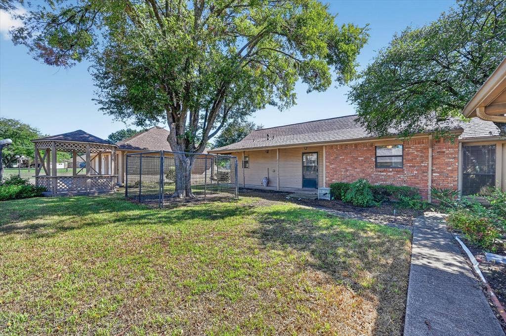 206 Harris Drive, Sunnyvale, TX 75182 Expansive green space featuring a wooden gazebo with a shingled roof, mature trees, a concrete pathway, and a brick-sided exterior