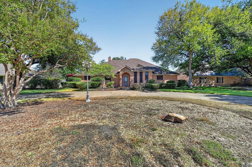 206 Harris Drive, Sunnyvale, TX 75182 Brick exterior, arched entryway, dark-colored front door, decorative shutters, and mature trees