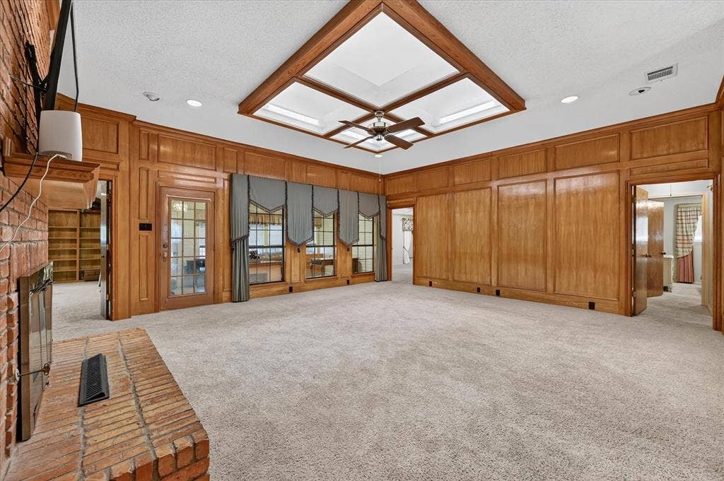 206 Harris Drive, Sunnyvale, TX 75182 Expansive room featuring wood paneling, a brick fireplace, built-in shelving, and a tray ceiling with a fan