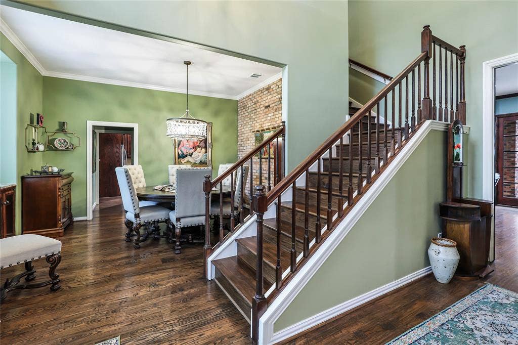 1204 Hills Creek Drive, McKinney, TX 75072 Hardwood flooring, wood staircase with dark balusters, crown molding, exposed brick accent wall, and a crystal chandelier