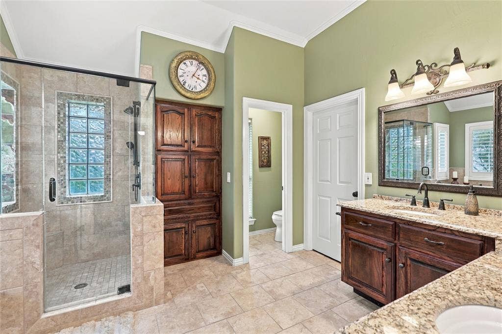 1204 Hills Creek Drive, McKinney, TX 75072 Tile flooring, glass-enclosed shower with tiled surround, built-in wood cabinetry, vanity with granite countertop, and mirror with overhead lighting