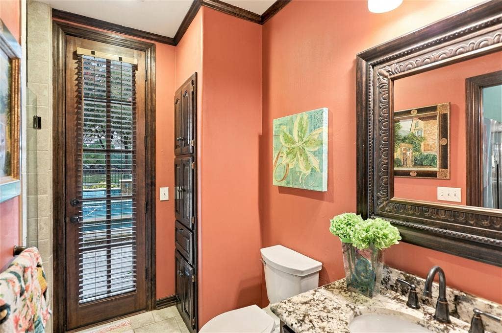 1204 Hills Creek Drive, McKinney, TX 75072 Granite-finish vanity with an undermount sink and dark bronze faucet, a built-in dark wood storage cabinet, and a full-light door with integrated blinds offering exterior access