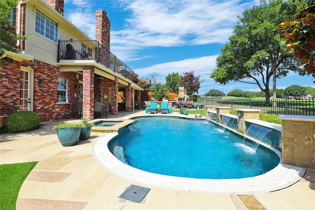 1204 Hills Creek Drive, McKinney, TX 75072 Expansive backyard featuring a curvilinear pool with integrated water features, a built-in spa, and a covered patio