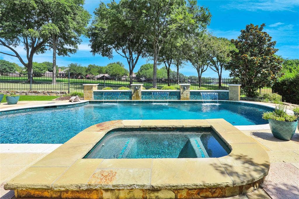 1204 Hills Creek Drive, McKinney, TX 75072 Swimming pool with an integrated spa, featuring stone coping and a tiled water wall with multiple water features