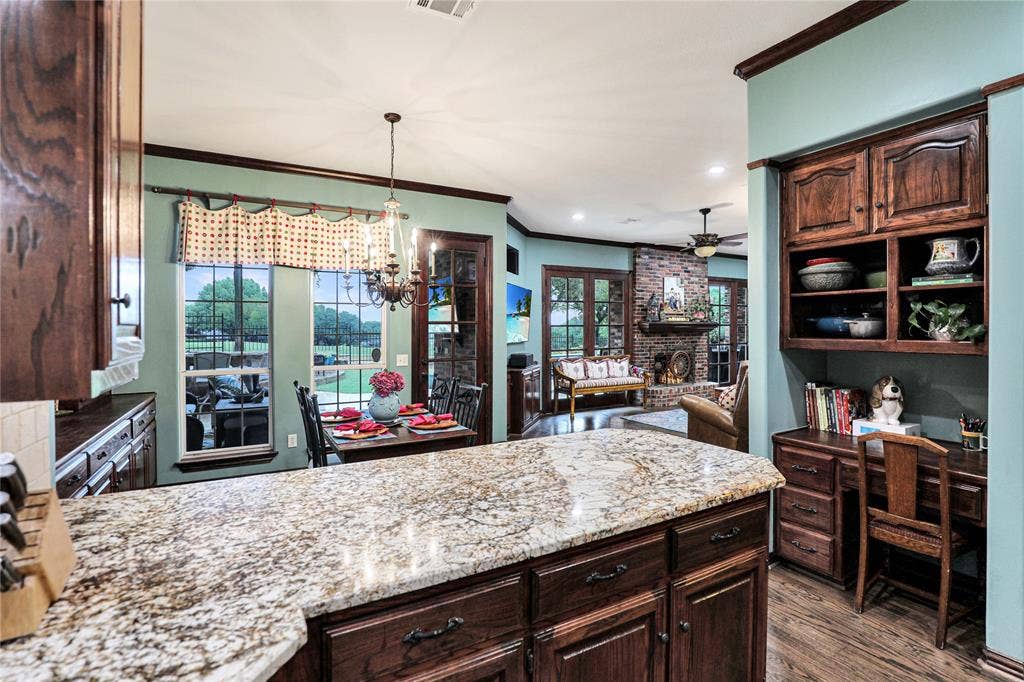 1204 Hills Creek Drive, McKinney, TX 75072 Kitchen island with a granite countertop, rich wood cabinetry, and wood-finish flooring