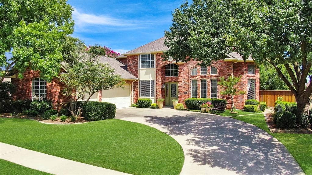 1204 Hills Creek Drive, McKinney, TX 75072 Brick exterior with multiple arched windows, mature landscaping, an attached garage, and a curved driveway
