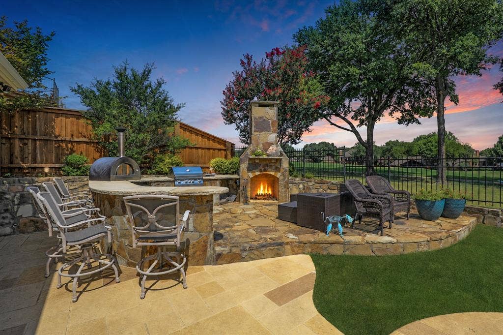 1204 Hills Creek Drive, McKinney, TX 75072 Expansive outdoor space featuring a stone-clad fireplace, built-in outdoor kitchen with pizza oven, flagstone patio, and manicured lawn