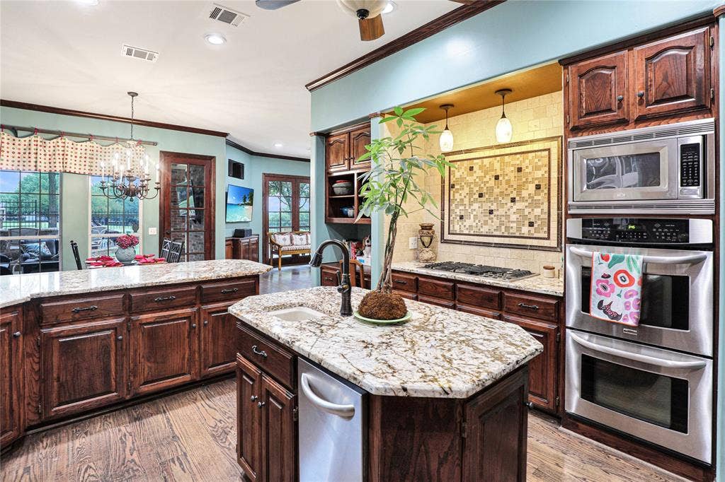 1204 Hills Creek Drive, McKinney, TX 75072 Gourmet kitchen featuring granite countertops, dark wood cabinetry, a gas cooktop, built-in stainless steel double ovens, and a mosaic tile backsplash