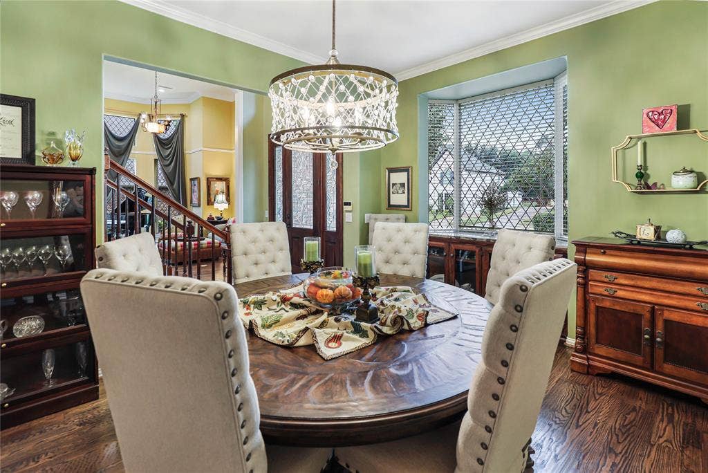 1204 Hills Creek Drive, McKinney, TX 75072 Wood-finish flooring, bay window with decorative security screen, detailed ceiling fixture, built-in display cabinetry, and a carved wood dining table