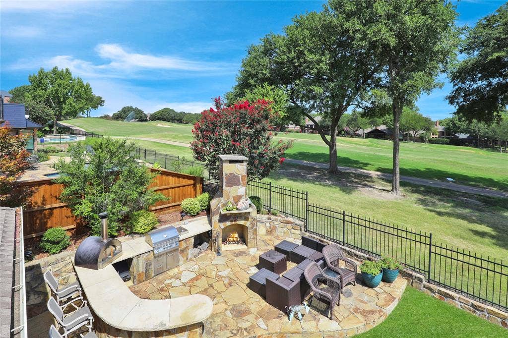 1204 Hills Creek Drive, McKinney, TX 75072 Stone-paved patio featuring a built-in outdoor kitchen with grill and pizza oven, a stone fireplace, and a counter-height bar with seating