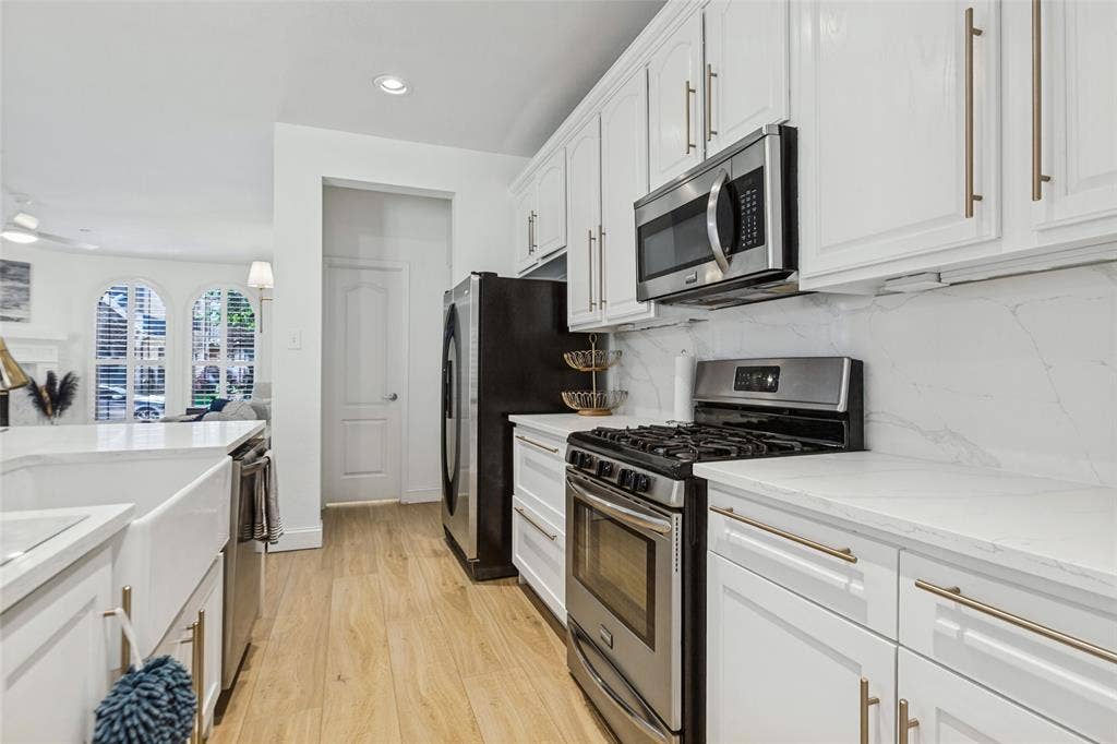6816 Livorno Lane, Frisco, TX 75034 White cabinetry with gold-tone hardware, stainless steel appliances, and light-toned wood-finish flooring, Private half bath tucked away