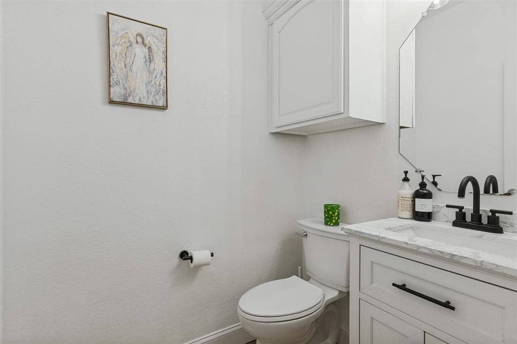 6816 Livorno Lane, Frisco, TX 75034 White shaker-style vanity with dark hardware, undermount sink, and stone-finish countertop Large private half bath downstairs