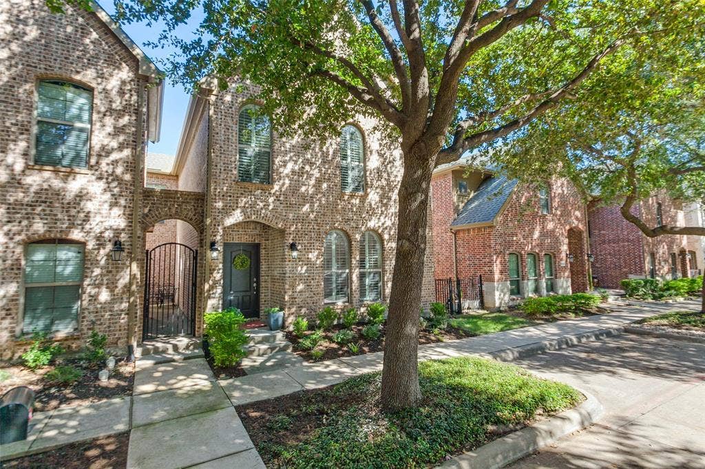 6816 Livorno Lane, Frisco, TX 75034 Brick exterior featuring arched windows with shutters, a stone walkway, and established trees with additional guest street parking