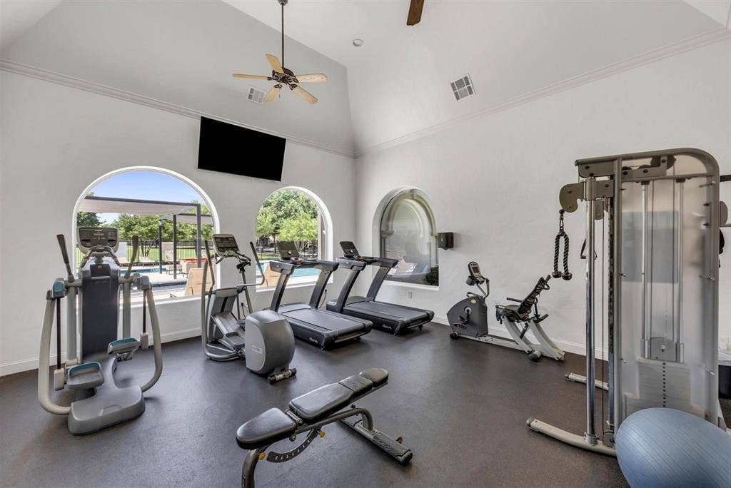 6816 Livorno Lane, Frisco, TX 75034 Fitness center featuring vaulted ceilings, arched windows, built-in television, and rubber flooring