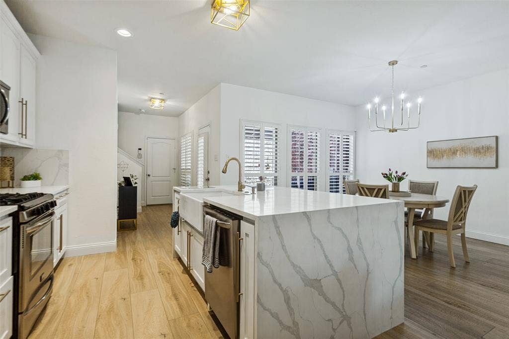 6816 Livorno Lane, Frisco, TX 75034 Open-concept kitchen and dining area featuring a waterfall island with an undermount farmhouse sink, stainless steel appliances, light wood-finish flooring, and white cabinetry