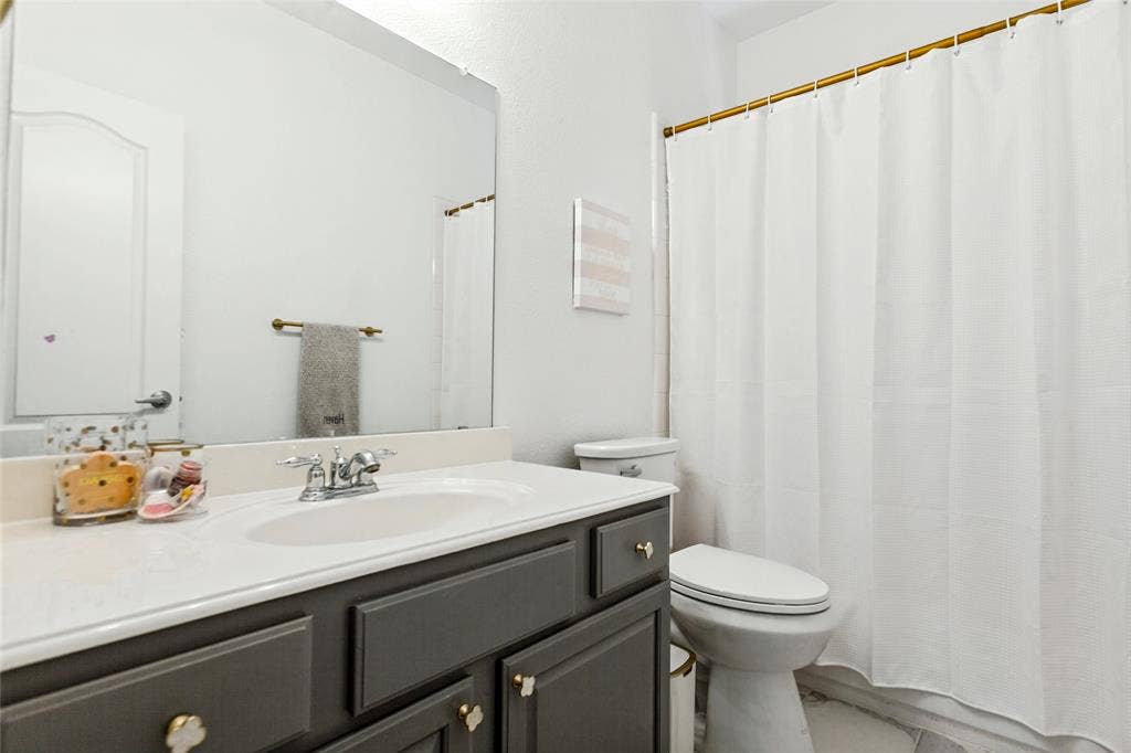 6816 Livorno Lane, Frisco, TX 75034 secondary bathroom with newly tiled floors, White vanity countertop with an integrated sink, dual-handle chrome faucet, and gray cabinetry