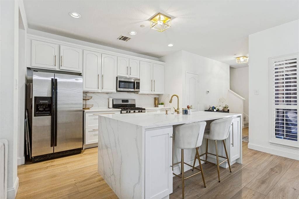 6816 Livorno Lane, Frisco, TX 75034 Gourmet kitchen featuring white custom cabinetry, stainless steel appliances, a center island with waterfall-edge quartz countertop, and wide luxury vinyl plank wood-finish flooring