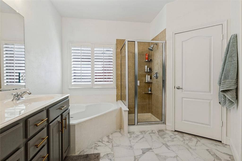 6816 Livorno Lane, Frisco, TX 75034 New White marble-look flooring, built-in jetted soaking tub, glass-enclosed shower with tile surround, vanity with dark cabinetry, and interior plantation shutters