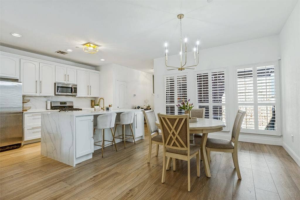 6816 Livorno Lane, Frisco, TX 75034 Contemporary kitchen featuring a large island with waterfall edge, white cabinetry, stainless steel appliances, and a gas range