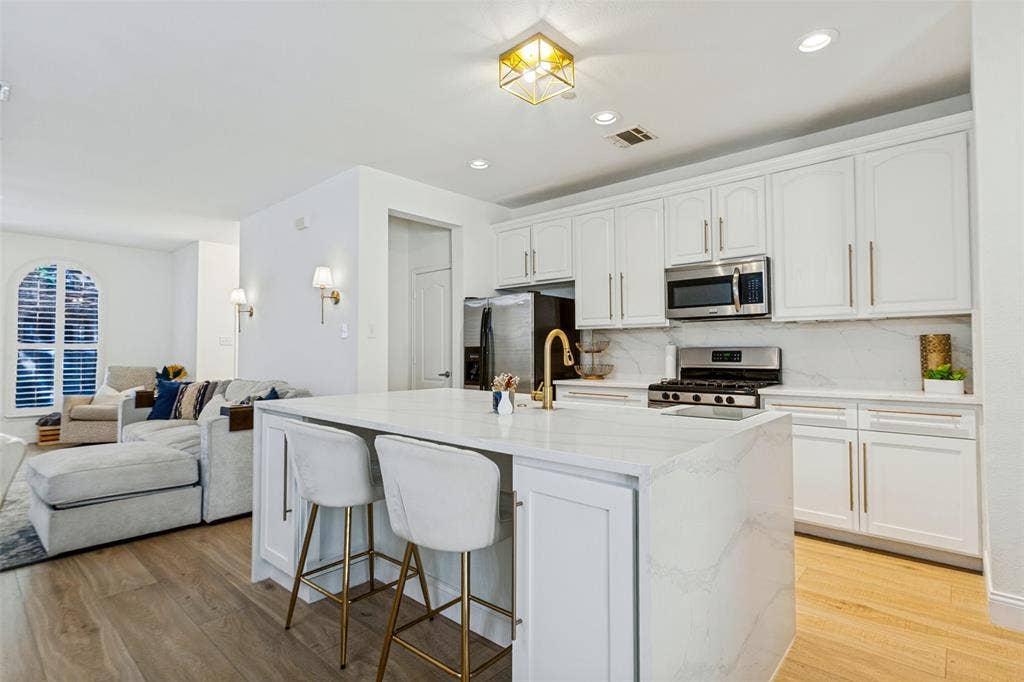 6816 Livorno Lane, Frisco, TX 75034 Open-concept kitchen with white cabinetry, stainless steel appliances, and a central island featuring a gold-finish faucet