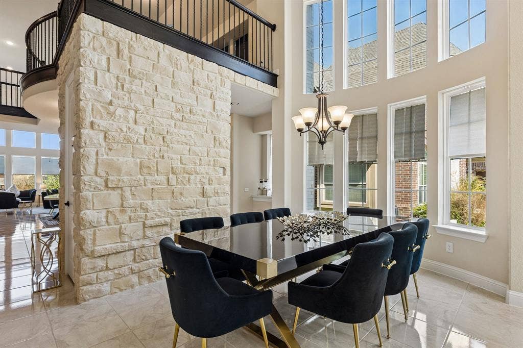 3613 Sparkling Drive, Plano, TX 75074 Two-story stone accent wall, upper-level balcony with dark wood railing, two-story window array, tile flooring, and an ornate chandelier