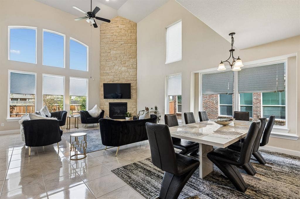 3613 Sparkling Drive, Plano, TX 75074 Vaulted ceiling with an integrated ceiling fan, stone-clad fireplace, large-format tile flooring, and multiple windows