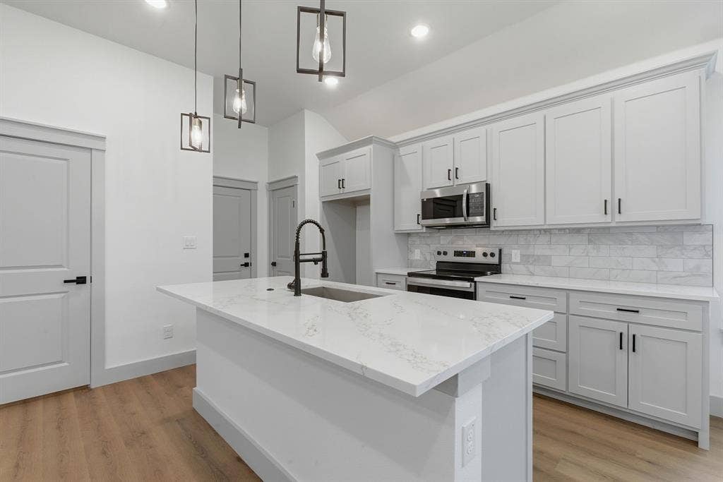 14583 Cherokee Lane, Log Cabin, TX 75148 Kitchen featuring an island with a built-in sink, white countertops, light gray cabinetry with black hardware, a stainless steel microwave, and wood-finish flooring