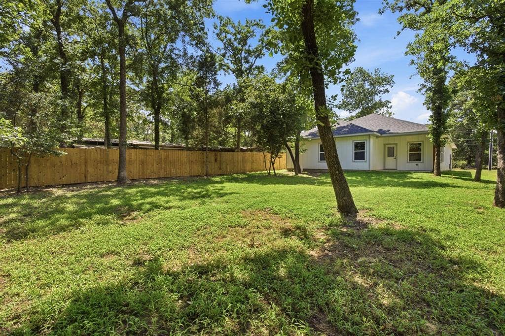 14583 Cherokee Lane, Log Cabin, TX 75148 Expansive backyard featuring a new wood privacy fence, mature trees, and a white exterior residence with multiple windows and a shingled roof