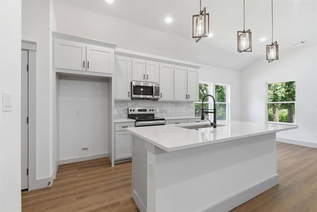 14583 Cherokee Lane, Log Cabin, TX 75148 Kitchen featuring a large island with sink, stainless steel microwave, white shaker-style cabinetry, wood-finish flooring, and vaulted ceiling