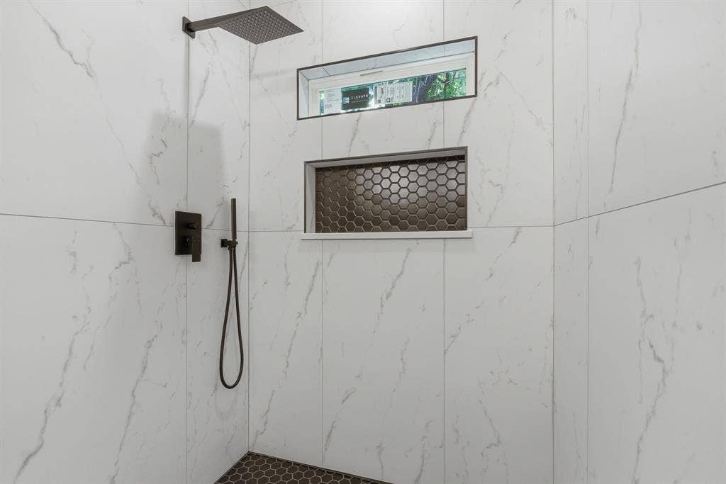 14583 Cherokee Lane, Log Cabin, TX 75148 Shower featuring large format white tile walls, a matte black rain shower head, a matte black handheld shower, a built-in shower niche with hexagonal tile, and a privacy window