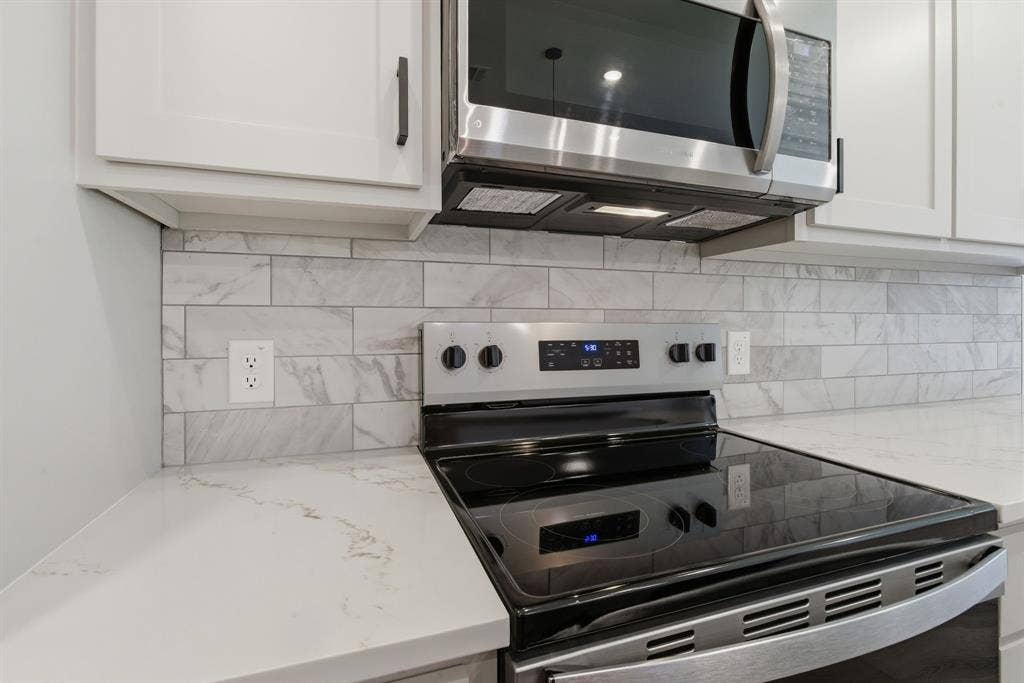 14583 Cherokee Lane, Log Cabin, TX 75148 White cabinetry with dark hardware, subway tile backsplash, light-toned countertop, stainless steel microwave, and stainless steel range