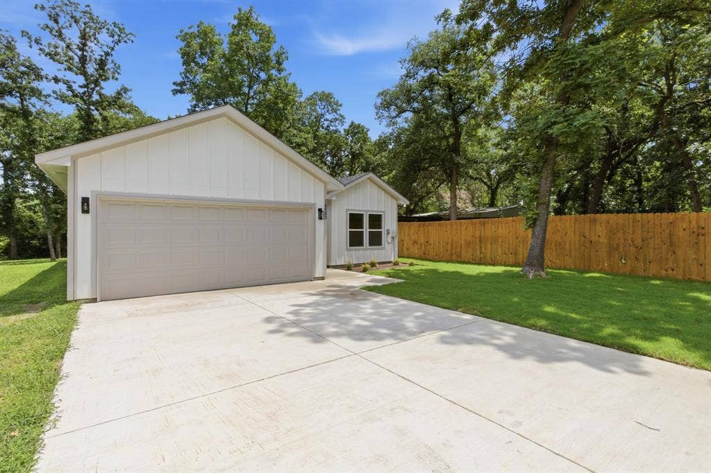 14583 Cherokee Lane, Log Cabin, TX 75148 White board and batten siding, attached two-car garage with light gray door, concrete driveway, and natural wood privacy fence