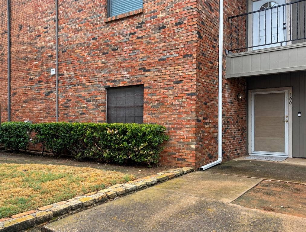 Red brick exterior with white downspout, ground-level entry, and an upper-level balcony with black railing