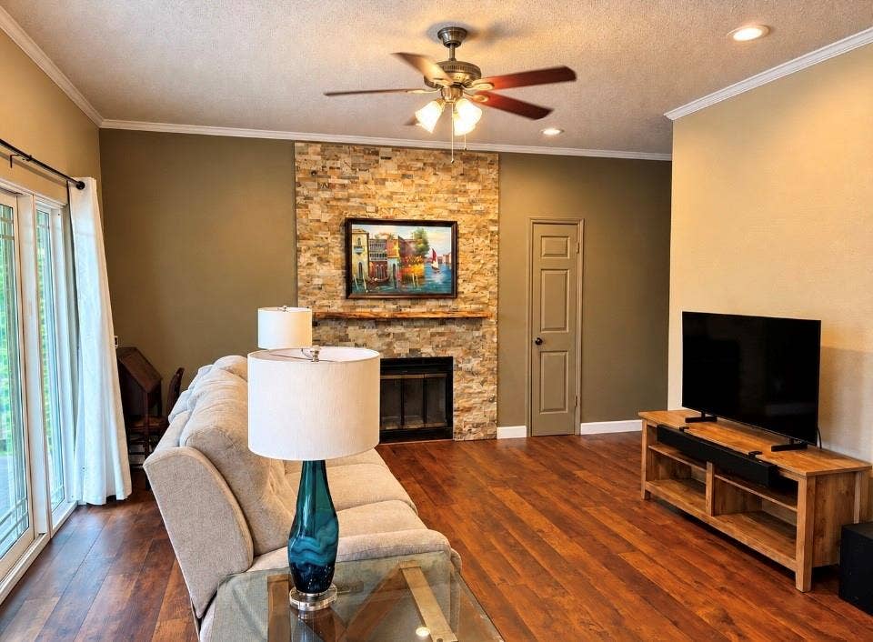 Spacious living area featuring wood-finish flooring, a stone-clad fireplace, and recessed lighting