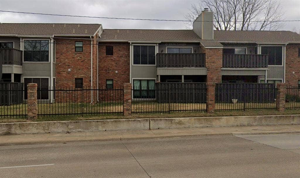 Brick and siding exterior with multiple balconies, a chimney feature, and a wrought iron fence with brick pillars
