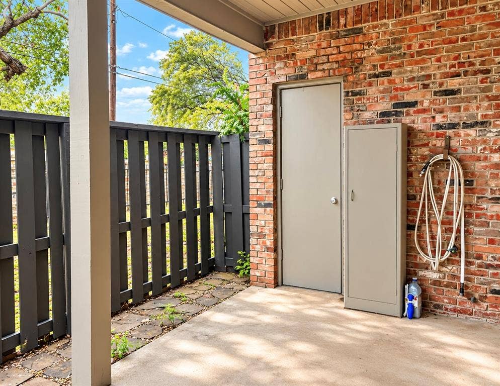 Brick exterior wall, covered patio, privacy fencing, concrete flooring, and an exterior storage cabinet