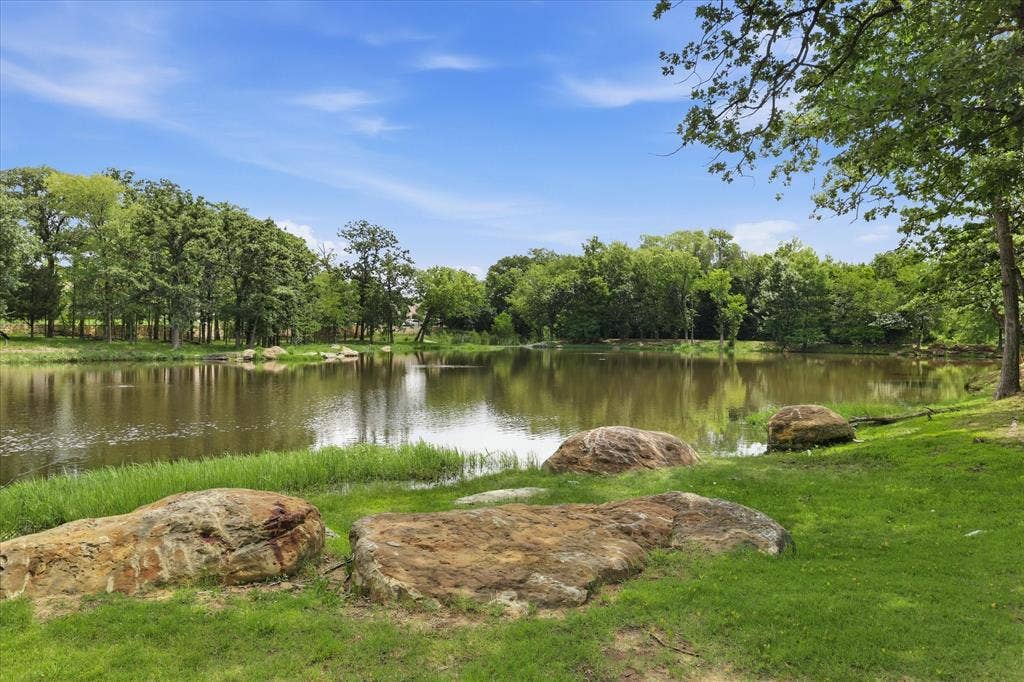 Expansive pond surrounded by lush green grass, mature trees, and natural rock formations