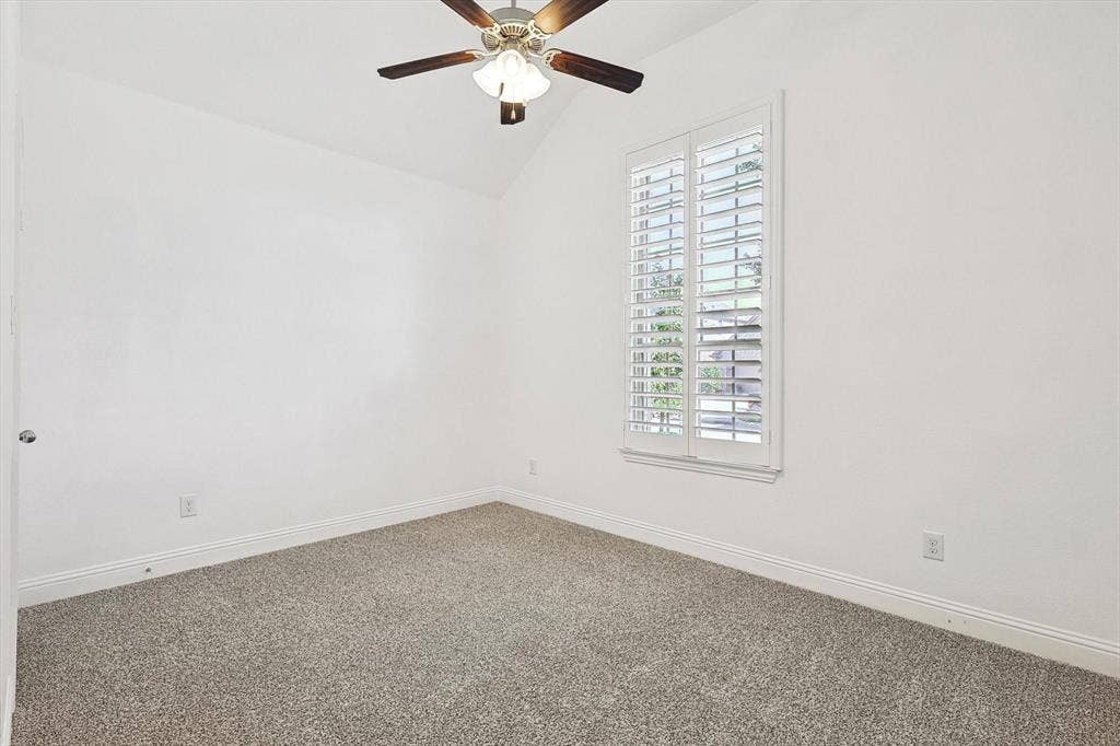 Vaulted ceiling with a ceiling fan, window with white plantation shutters, and light-toned carpet flooring