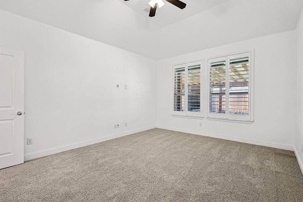 Neutral-toned carpeting, white walls, and a vaulted ceiling with a ceiling fan