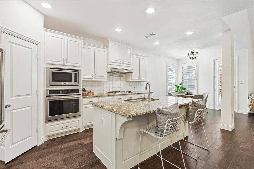 Kitchen featuring an island with stone countertop, built-in stainless steel appliances, white cabinetry, dark wood-finish flooring, and recessed lighting